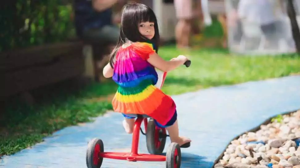 girl riding a red tricycle on a small blue road in a playground