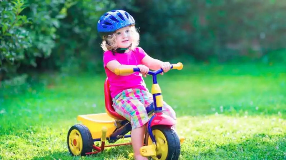 toddler girl riding her tricycle wearing a safety helmet enjoying a nice sunny day