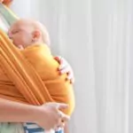 young mother with little baby in sling at home