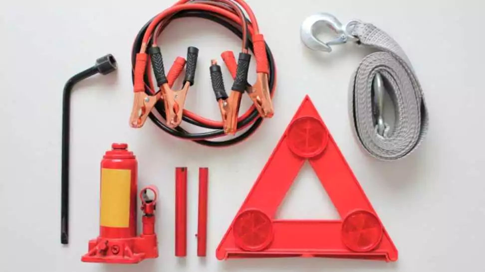 basic emergency kit for a car consisting of a bottle jack wheel spanner tow rope red triangles and jumper cables