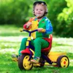 cute boy wearing safety helmet riding his tricycle in sunny summer park