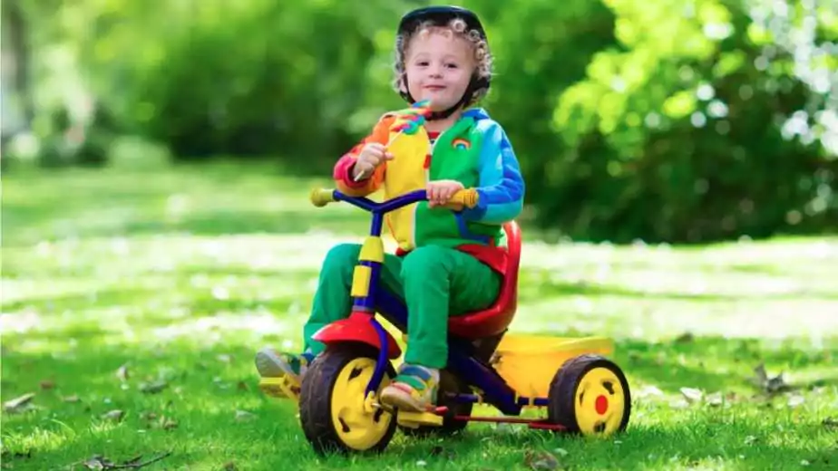 cute boy wearing safety helmet riding his tricycle in sunny summer park