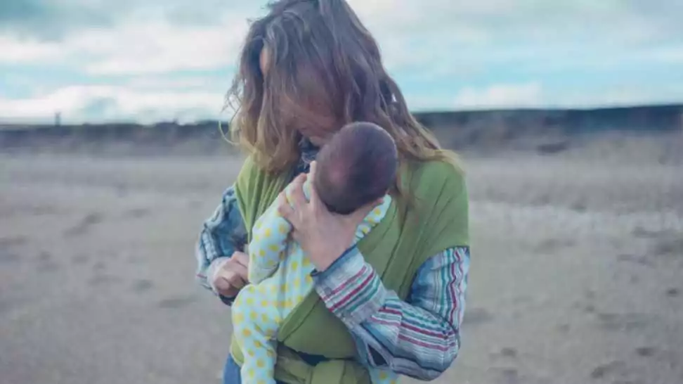 a young mother on the beach is putting her baby in a wrap