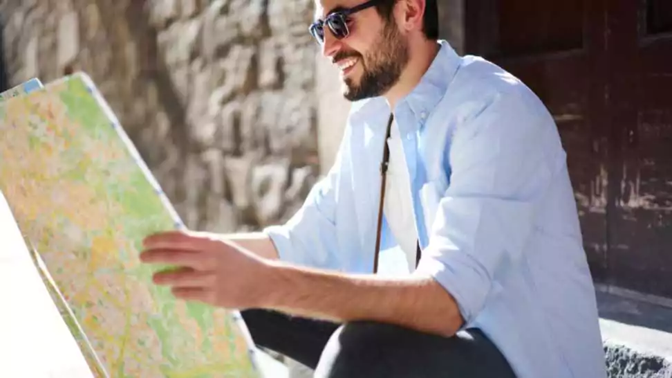 male in casual clothes and sunglasses sitting on stairs outside and looking at road map