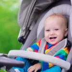 baby boy in warm colorful knitted jacket sitting in modern stroller on a walk in a park