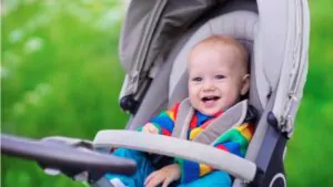 baby boy in warm colorful knitted jacket sitting in modern stroller on a walk in a park