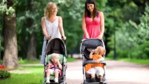 happy mothers walking together with kids in baby strollers