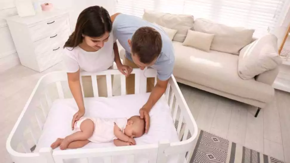happy couple near crib with their cute baby at home