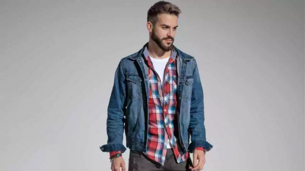 casual man wearing denim jacket standing and posing with style on gray studio background