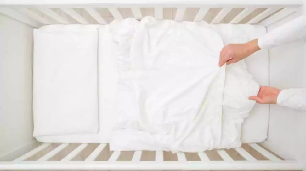 young adult mother hands changing white blanket cover in baby crib