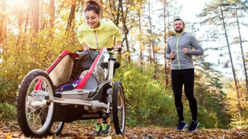 beautiful young family with baby in jogging stroller running outside in autumn nature