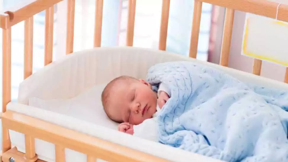 new born child in wooden co sleeper crib