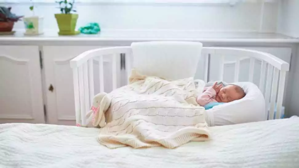 newborn baby girl having a nap in co sleeper crib attached to parents' bed