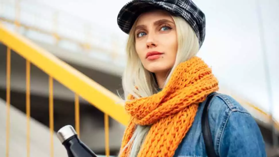 portrait of young blonde teenager girl wearing blue denim jacket with orange scarf and plaid cap