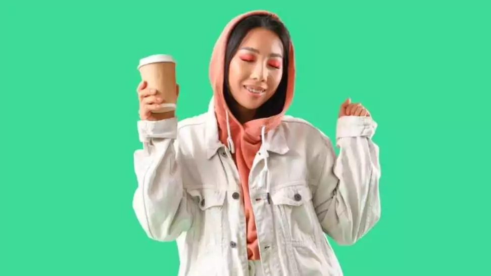 young asian woman in hoodie and cotton jacket with coffee cup on green background