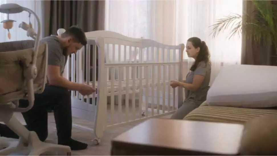 loving parents together assembling white crib for newborn baby at nursery