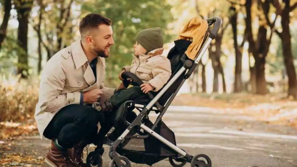 father with little son walking in baby stroller in autumnal park