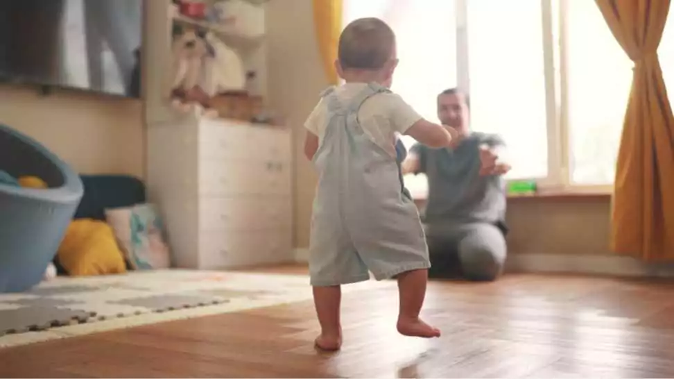 a baby learning to walk and takes first steps towards his father