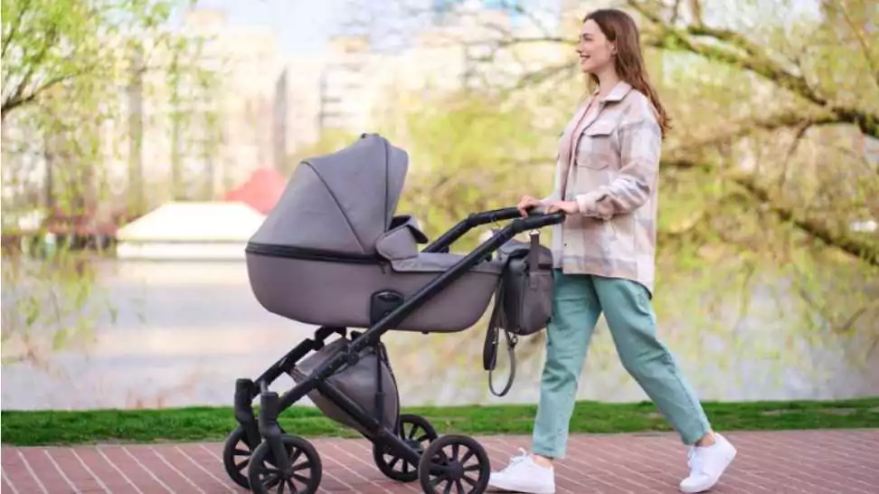 beautiful smiling young mother pushing stroller with little baby walking in spring park