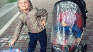 sister with umbrella and younger brother sitting in an umbrella stroller with rain protection cover
