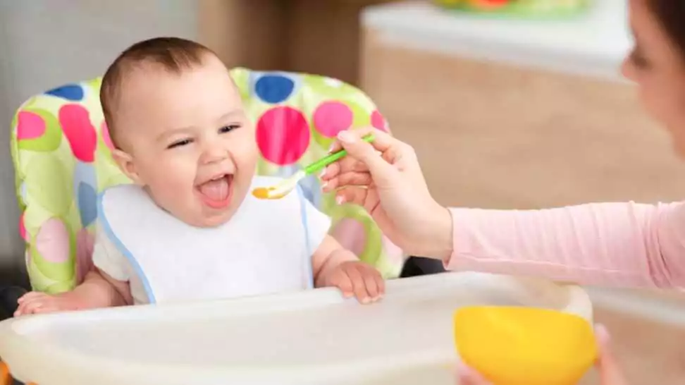 mother giving healthy food to her adorable baby child sitting on a high chair