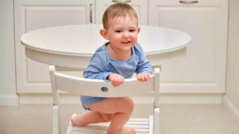 toddler baby climbs onto a chair at the kitchen white table