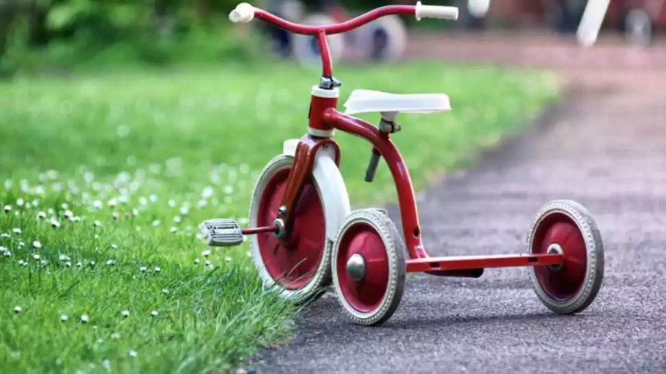 red kids tricycle on a road near green grass