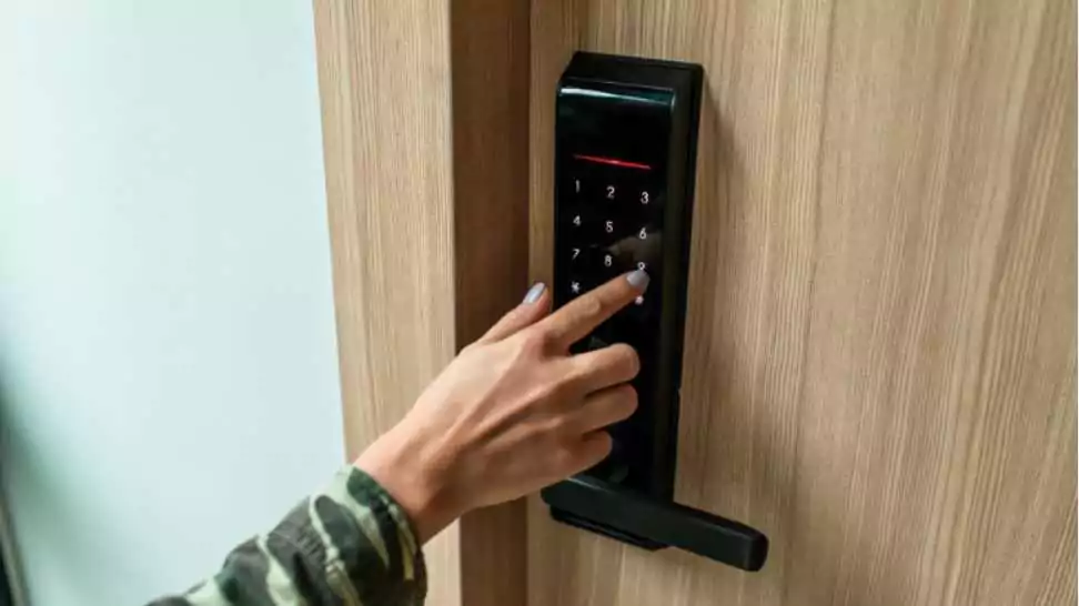 closeup of a woman's finger entering password code on the smart digital touch screen keypad entry door lock in front of the room