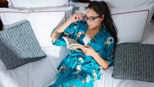 beautiful and attractive young girl lying in bed and reading a book the girl wears a comfortable night dress with flowers in turquoise color