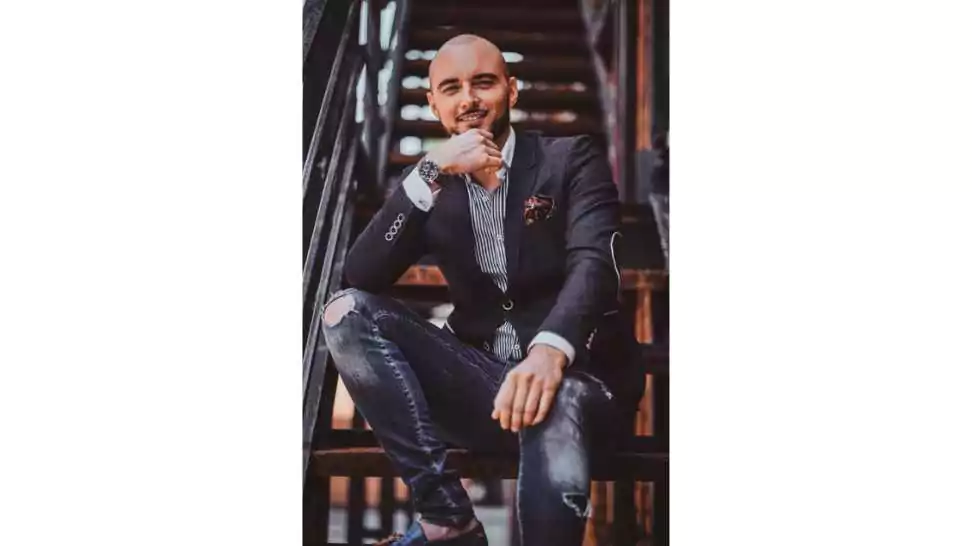 smiling attractive man in blazer and ripped jeans sitting on the stair
