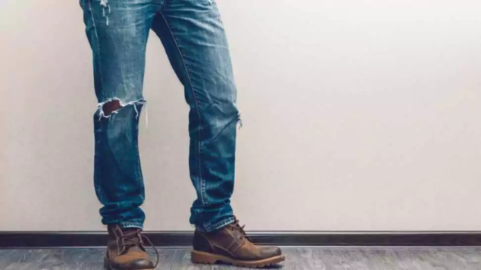 young fashion man's legs wearing ripped jeans and boots on wooden floor