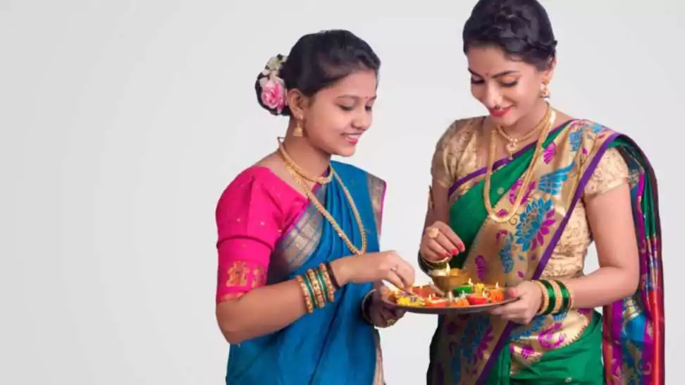 two maharashtrian girls celebrating festival in nauvari saree holding a puja thali with oil lamps in it