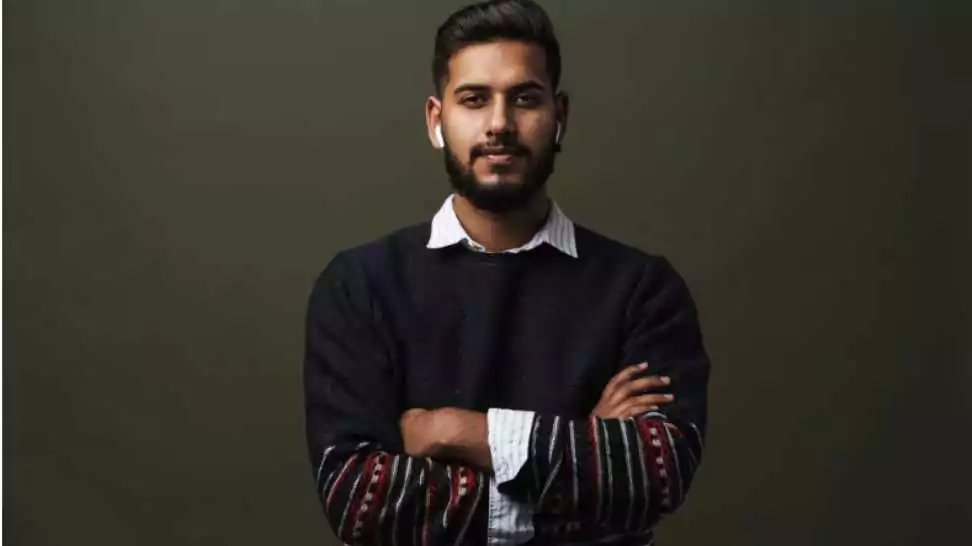 portrait of young bearded calm indian man with folded hands wearing pullover over the shirt