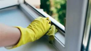 a person wearing gloves washes the window frame with a cleaning cloth